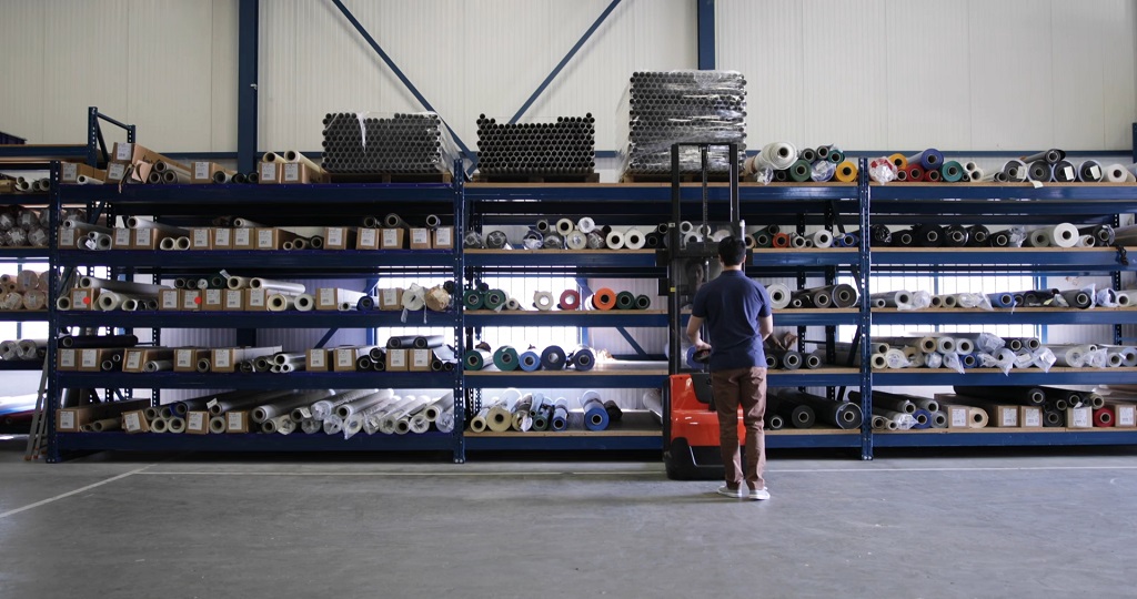 A worker stands in front of industrial shelves stacked with packaging materials inside a warehouse
